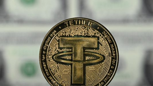 An illustration picture taken in London on May 8, 2022, shows a gold plated souvenir cryptocurrency Tether (USDT) coin arranged beside a screen displaying US dollar notes. - Tether (USDT) is an Ethereum token known as a stablecoin that is pegged to the value of the US dollar, and is currently the largest stablecoin with a market value of USD 83 billion dollars. (Photo by Justin TALLIS / AFP) (Photo by JUSTIN TALLIS/AFP via Getty Images)